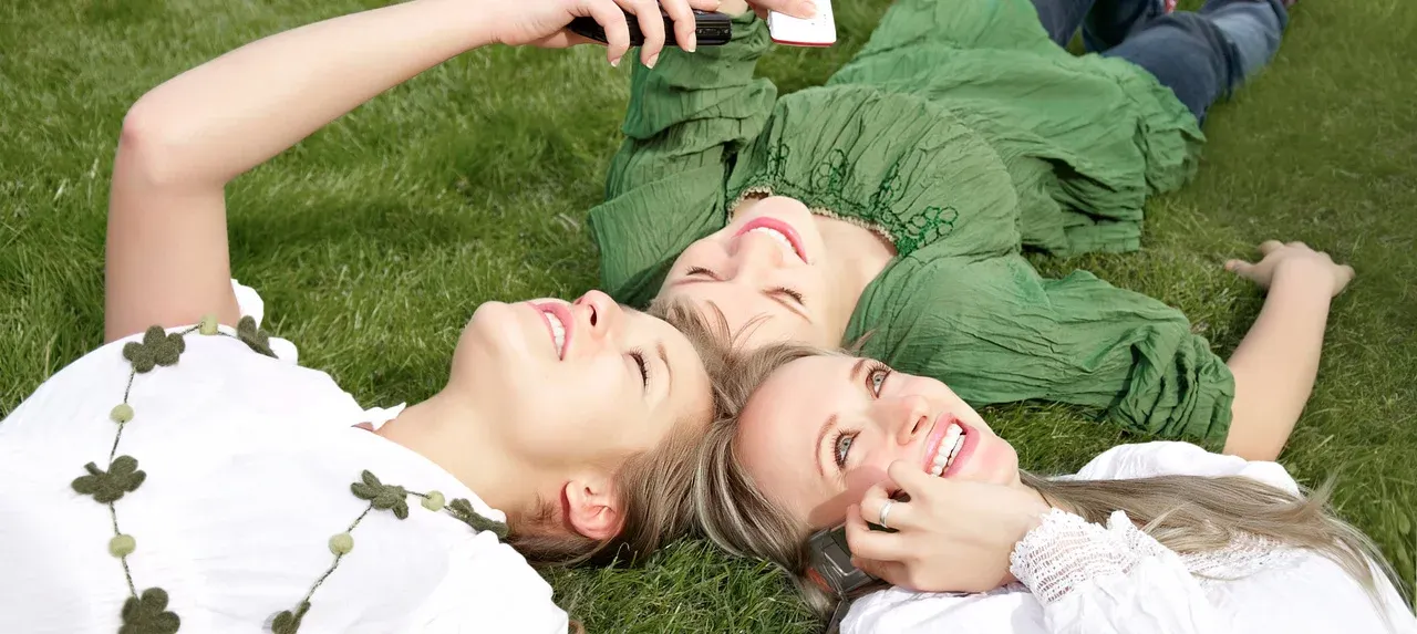 Drei Frauen liegen auf einer Wiese und telefonieren